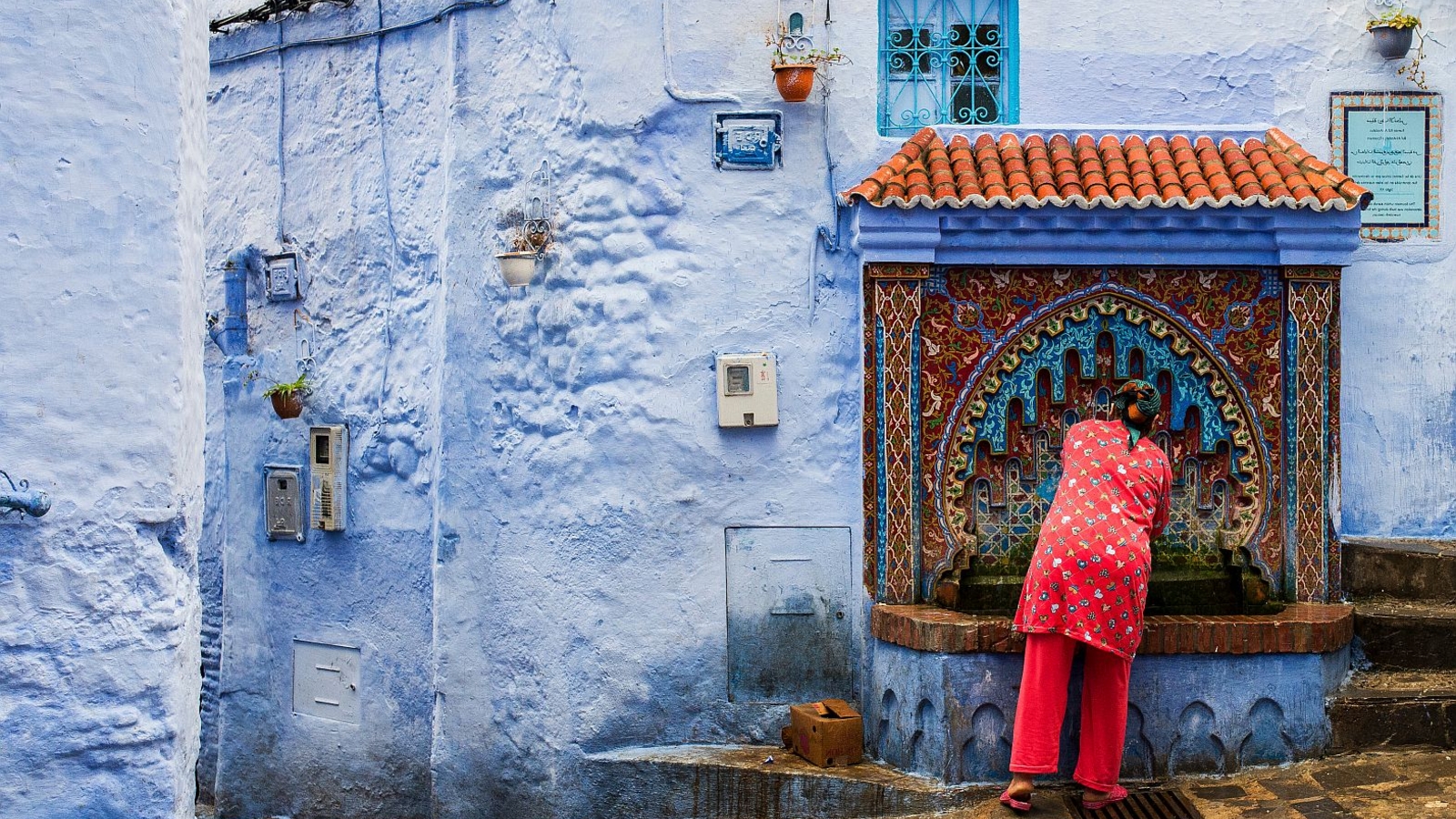 Woman collecting water from a fountain, Chefchaouen, Morocco. Photo: Miguel- AdobeStock.com